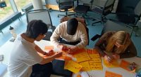 Eine Gruppe von Drei Menschen sitzen zusammen und machen Design Thinking