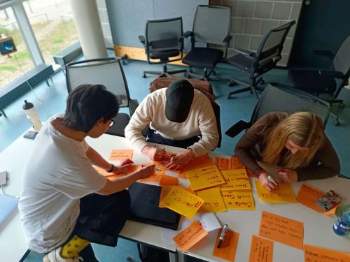Eine Gruppe von Drei Menschen sitzen zusammen und machen Design Thinking
