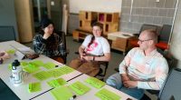 Eine Gruppe von Drei Menschen sitzen zusammen und machen Design Thinking